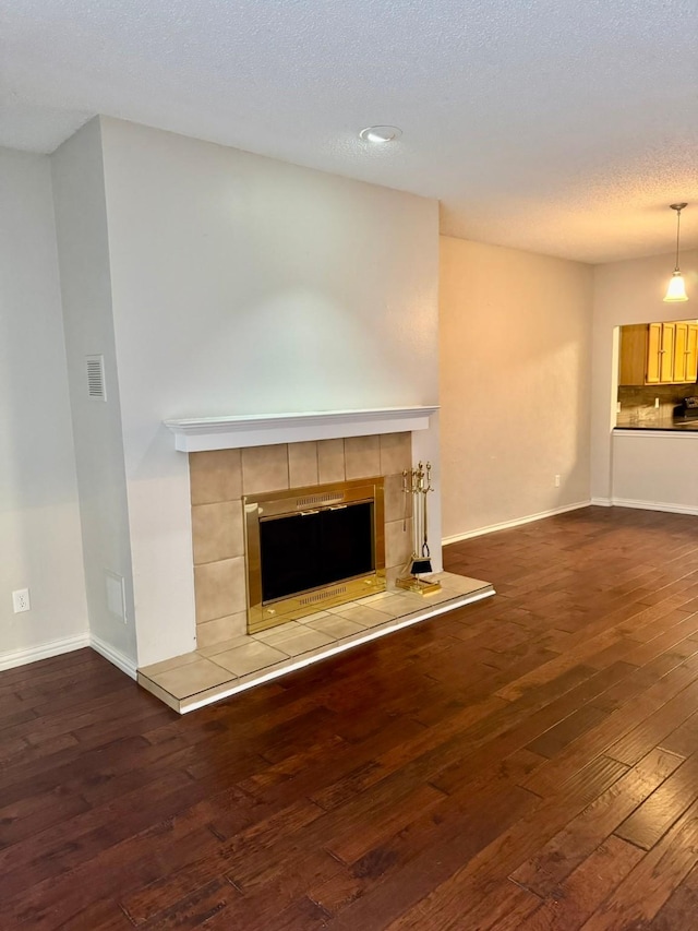 unfurnished living room with wood-type flooring, a textured ceiling, and a tiled fireplace