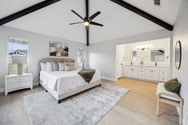 bedroom featuring beam ceiling, light wood-type flooring, ensuite bath, and ceiling fan