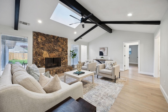 living room with ceiling fan, light hardwood / wood-style floors, lofted ceiling with skylight, and a fireplace