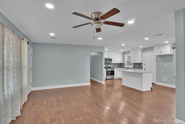 kitchen featuring hardwood / wood-style flooring, appliances with stainless steel finishes, a center island, tasteful backsplash, and white cabinets