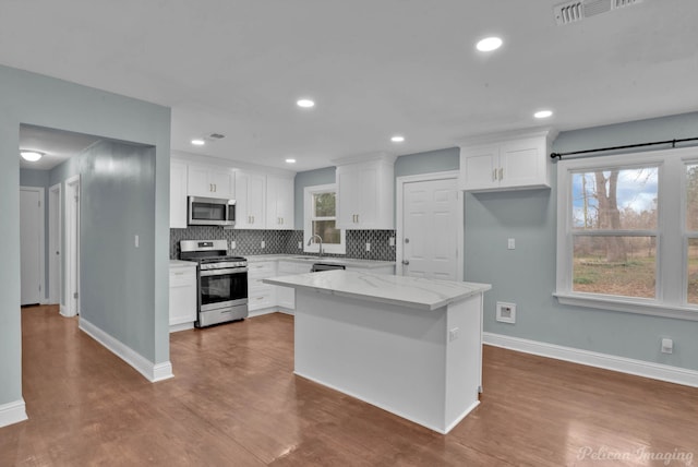 kitchen with light stone countertops, appliances with stainless steel finishes, white cabinets, and backsplash