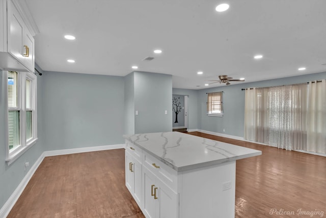 kitchen featuring white cabinetry, light stone counters, a center island, light wood-type flooring, and ceiling fan