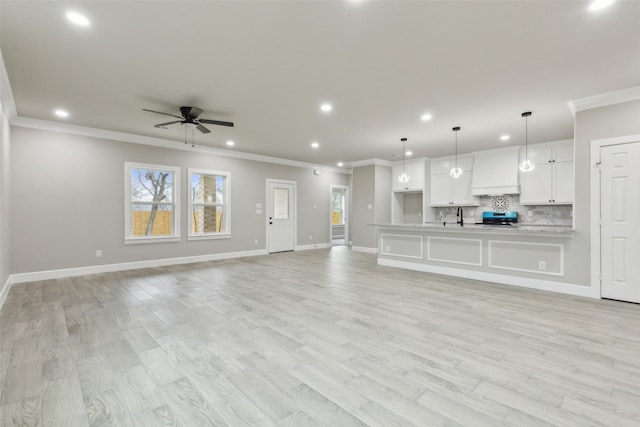 unfurnished living room with ceiling fan, sink, light hardwood / wood-style floors, and ornamental molding