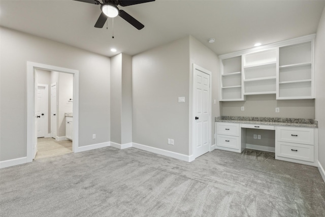 unfurnished office with light carpet, built in desk, and ceiling fan