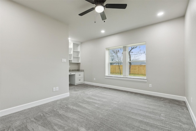 unfurnished living room with ceiling fan, built in desk, and light carpet