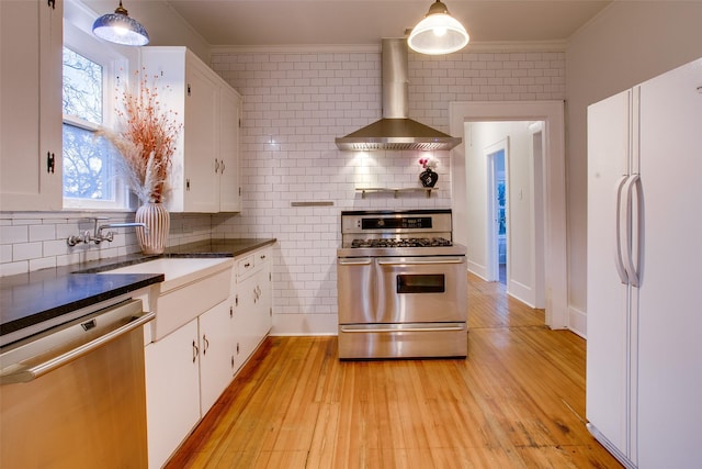 kitchen featuring white cabinetry, stainless steel appliances, wall chimney range hood, pendant lighting, and light wood-type flooring