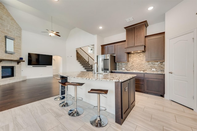 kitchen featuring stainless steel refrigerator, a kitchen breakfast bar, an island with sink, lofted ceiling, and light wood-type flooring