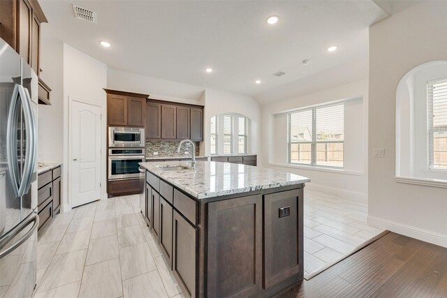 kitchen with a center island with sink, sink, light hardwood / wood-style flooring, light stone counters, and stainless steel appliances