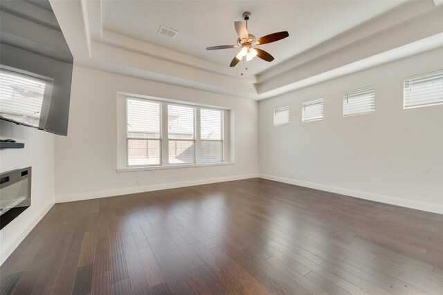 unfurnished living room featuring dark hardwood / wood-style floors, ceiling fan, and a tray ceiling