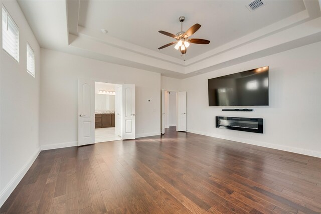 unfurnished living room featuring dark hardwood / wood-style floors, ceiling fan, and a tray ceiling