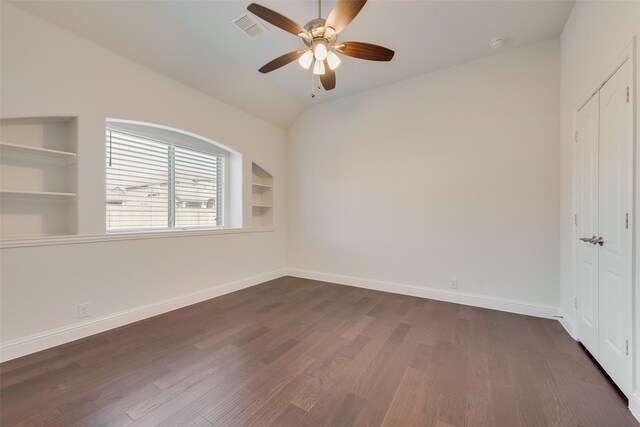 empty room with vaulted ceiling, dark hardwood / wood-style floors, built in features, and ceiling fan