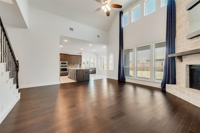 unfurnished living room with ceiling fan, a stone fireplace, dark hardwood / wood-style flooring, and high vaulted ceiling