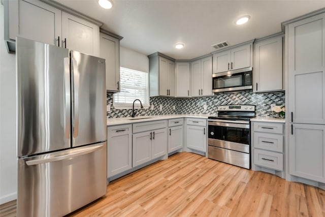 kitchen with gray cabinetry, sink, appliances with stainless steel finishes, tasteful backsplash, and light hardwood / wood-style floors