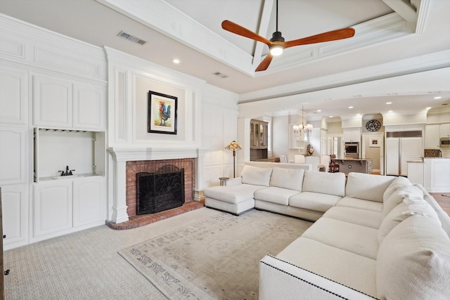 living room with a tray ceiling, ceiling fan, crown molding, and a brick fireplace