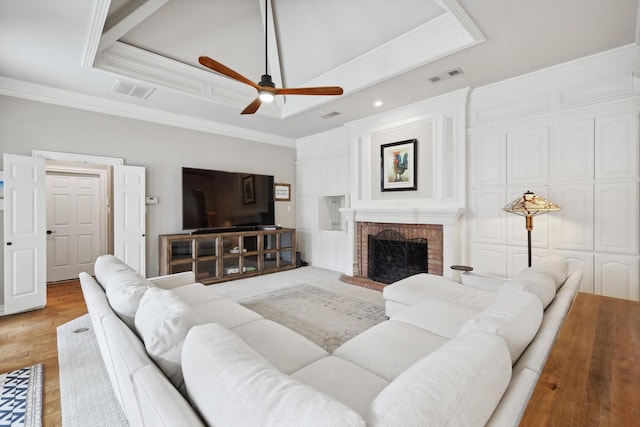 living room featuring a tray ceiling, ceiling fan, crown molding, and a brick fireplace