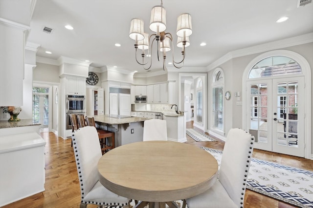 dining room featuring a chandelier, french doors, light hardwood / wood-style flooring, and crown molding