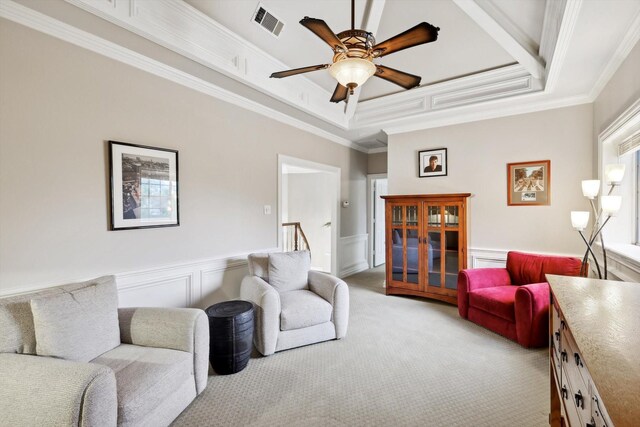 carpeted living room featuring a raised ceiling, ceiling fan, and ornamental molding