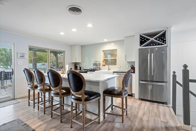 kitchen with backsplash, white cabinetry, light hardwood / wood-style floors, and appliances with stainless steel finishes