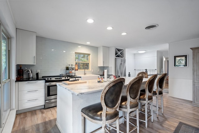 kitchen with white cabinets, decorative backsplash, light wood-type flooring, and stainless steel appliances