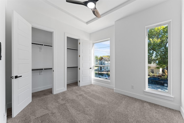 unfurnished bedroom featuring multiple windows, ceiling fan, carpet floors, and multiple closets