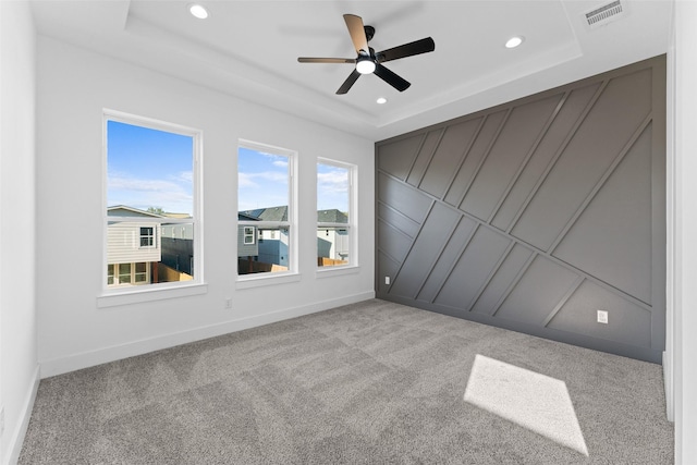 empty room featuring ceiling fan, light colored carpet, and a tray ceiling