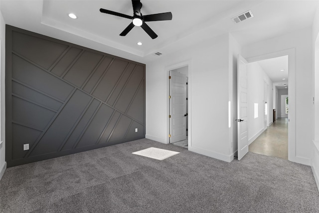 carpeted empty room with a raised ceiling and ceiling fan