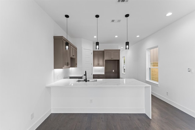 kitchen with kitchen peninsula, sink, hanging light fixtures, and dark wood-type flooring