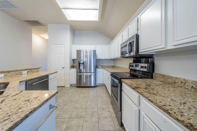 kitchen with light tile patterned flooring, white cabinetry, light stone counters, vaulted ceiling, and stainless steel appliances