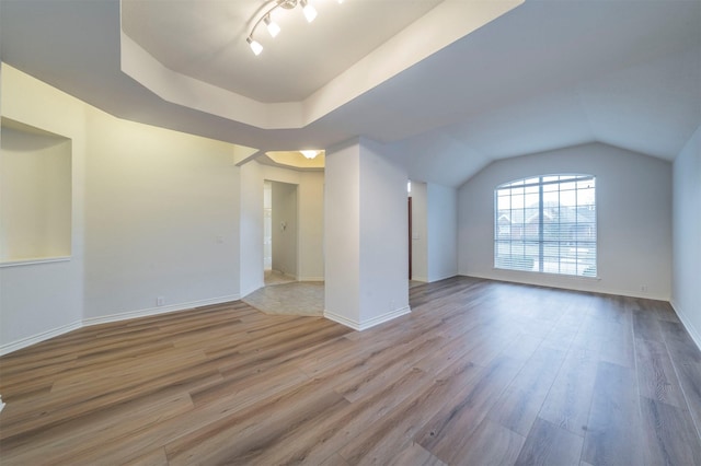 empty room with lofted ceiling, a tray ceiling, light hardwood / wood-style floors, and rail lighting