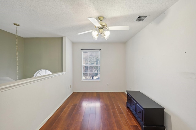 unfurnished room with a textured ceiling, ceiling fan, and dark wood-type flooring