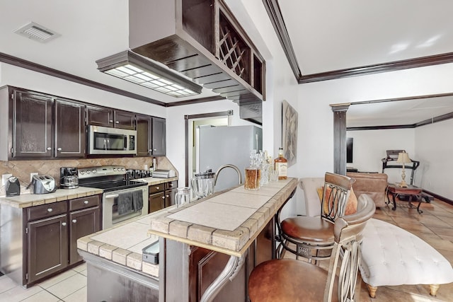 kitchen with dark brown cabinets, tile counters, stainless steel appliances, and a breakfast bar area