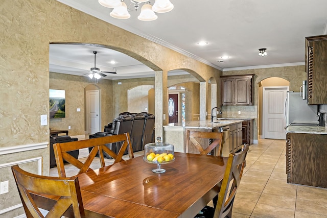 tiled dining area with sink, ceiling fan with notable chandelier, and ornamental molding