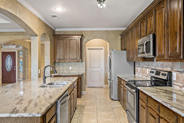 kitchen featuring stainless steel appliances, light stone counters, ornamental molding, and sink