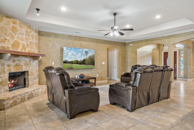 tiled living room featuring ceiling fan, a stone fireplace, a raised ceiling, and ornamental molding