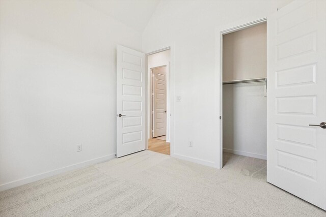 unfurnished bedroom with light colored carpet, a closet, and lofted ceiling