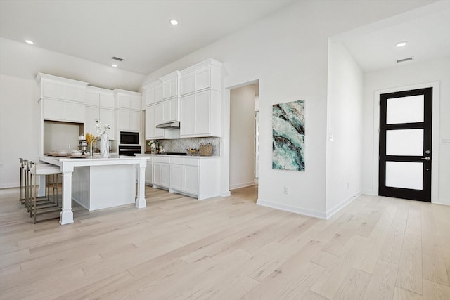 kitchen featuring a breakfast bar area, a center island with sink, white cabinets, black appliances, and light wood-type flooring