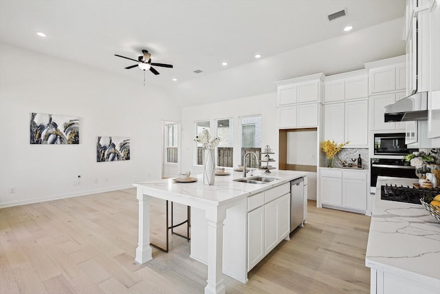 kitchen with light stone countertops, sink, black appliances, white cabinets, and an island with sink