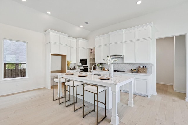 kitchen featuring a center island with sink, light hardwood / wood-style floors, white cabinetry, and black appliances