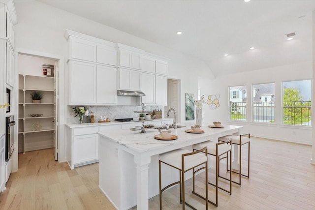 kitchen featuring an island with sink, appliances with stainless steel finishes, light hardwood / wood-style floors, light stone counters, and white cabinetry