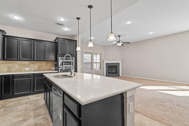 kitchen featuring sink, a center island with sink, a tiled fireplace, decorative backsplash, and decorative light fixtures