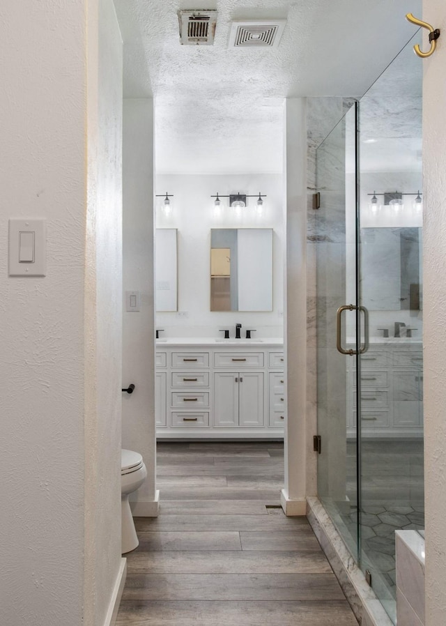 bathroom with vanity, toilet, a textured ceiling, walk in shower, and wood-type flooring