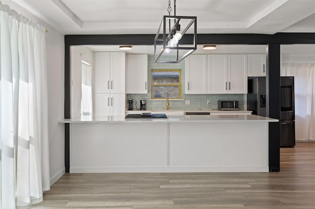 kitchen with appliances with stainless steel finishes, decorative light fixtures, white cabinetry, backsplash, and light wood-type flooring