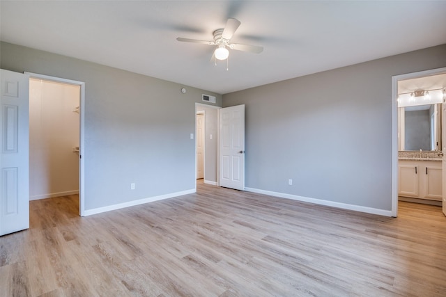 unfurnished bedroom with light hardwood / wood-style floors, ensuite bathroom, ceiling fan, and a walk in closet