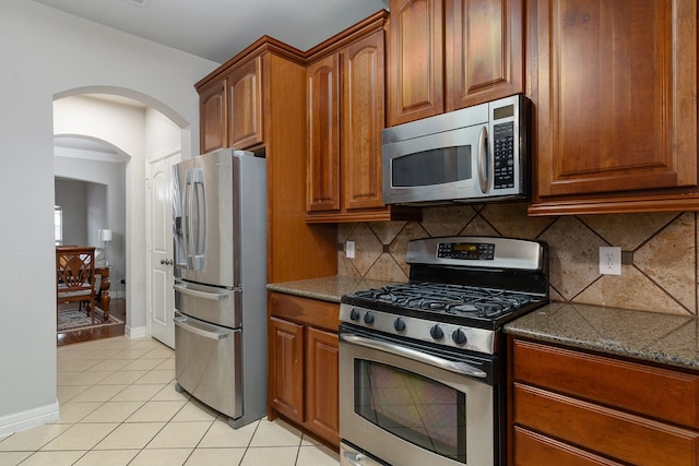 kitchen with dark stone countertops, crown molding, decorative backsplash, light tile patterned flooring, and appliances with stainless steel finishes