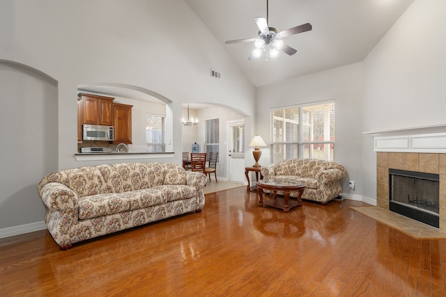 living room featuring high vaulted ceiling, hardwood / wood-style flooring, ceiling fan with notable chandelier, and a tile fireplace