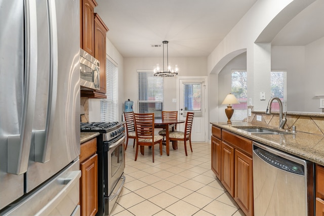 kitchen featuring light stone countertops, appliances with stainless steel finishes, sink, decorative light fixtures, and an inviting chandelier