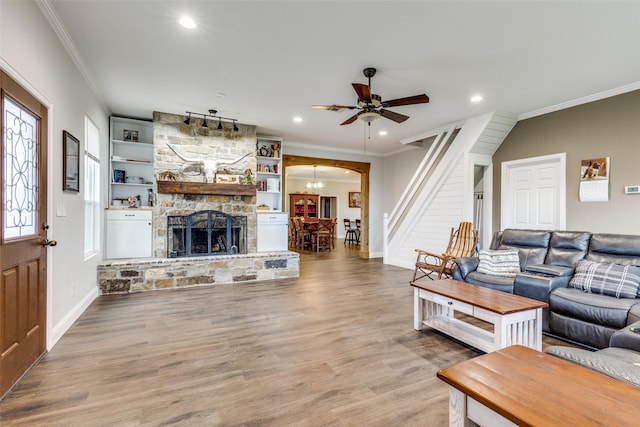 living room featuring hardwood / wood-style flooring, ornamental molding, a fireplace, and ceiling fan with notable chandelier