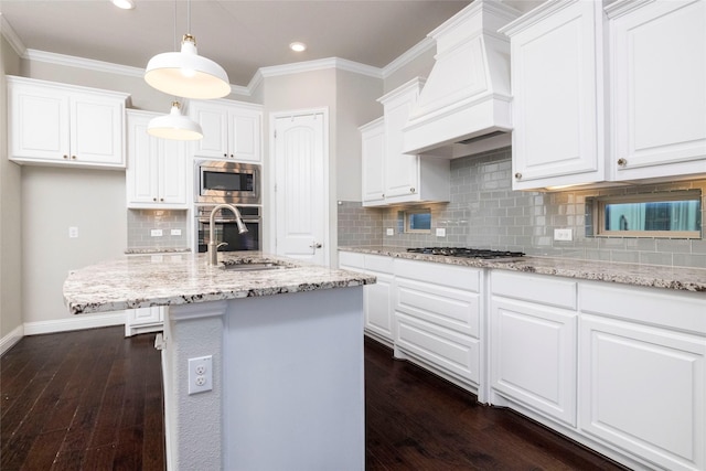 kitchen with appliances with stainless steel finishes, dark hardwood / wood-style flooring, premium range hood, a kitchen island with sink, and sink