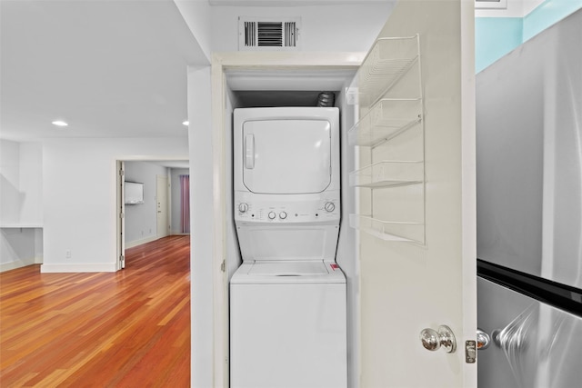 laundry room featuring wood-type flooring and stacked washing maching and dryer