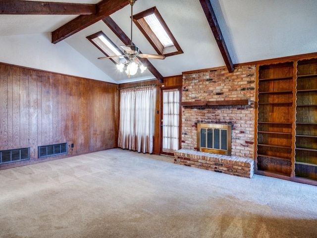 unfurnished living room with light colored carpet, lofted ceiling with skylight, ceiling fan, a fireplace, and wood walls